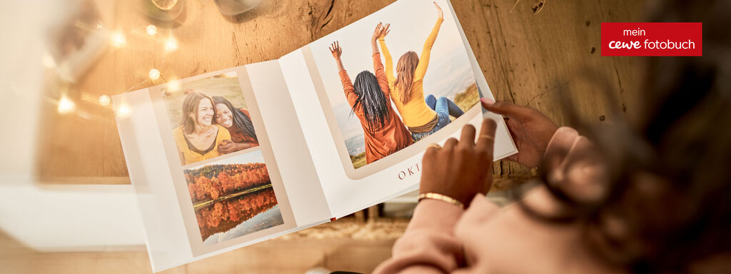 Jemand blättert an einem gemütlichen Tisch durch ein CEWE FOTOPRODUKT mit Fotos von Freunden.
